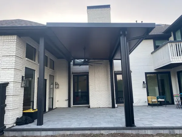 Full view of a black steel patio cover spanning a paver patio on a modern white brick home — CertiPro project